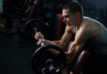 Man doing EZ barbell bicep exercises on Scott bench.